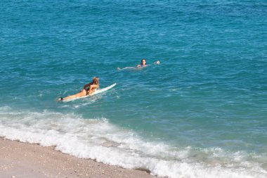 Saint-Gilles Bains, La Reunion - 13 Haziran 2017: Arkadaşı Plage des Roches Noires 'da yüzerken sörf tahtasındaki kız).