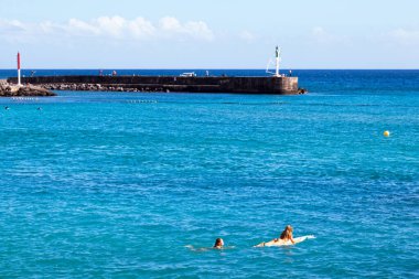 Saint Gilles Bains, La Reunion - 13 Haziran 2017: Arkadaşı Plage des Roches Noires 'ta arkasında yüzerken sörf tahtasındaki kız).