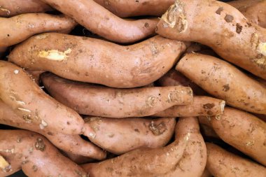 Close-up on a stack of sweet potatoes for sale on a market stall.