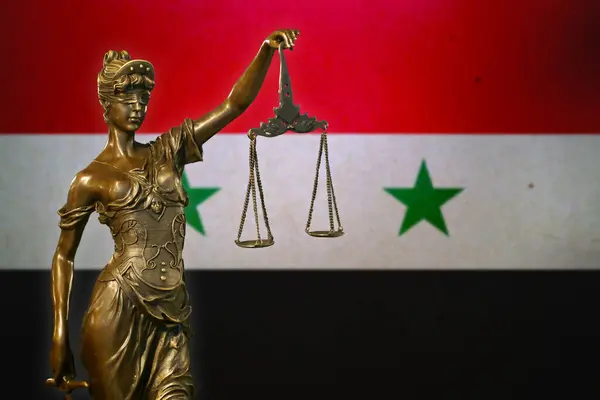 stock image Close-up of a small bronze statuette of Lady Justice before a flag of Syria.