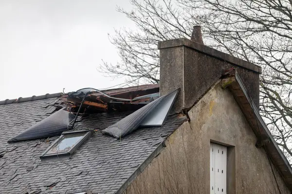 stock image Roof of a house damaged after the solar panels of the building opposite it were torn off and traveled about 50 meters at 106 mph during an autumn storm, ending up embedded near the chimney.