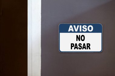 Blue and white notice sign on the side of an open door stating in Spanish 