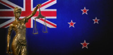Yeni Zelanda bayrağı önünde küçük bronz bir Adalet Heykeli..