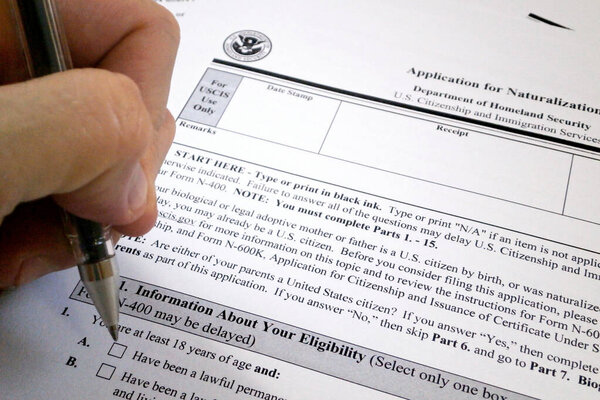 A pen hold by the fingers of somebody ready to fill an application for U.S. naturalization form.