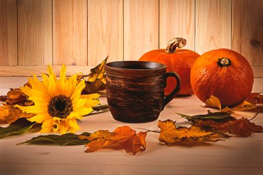Eski bir fincan kahve, portakal kabakları, sonbahar yaprakları ve ahşap ışıklı arka planda bir ayçiçeği. Cadılar Bayramı için kompozisyon.
