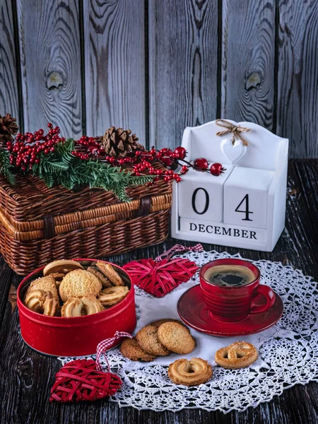 Cookies in a red box and a red cup of coffee and a calendar on the table. Concept for National Cookie Day, December 4. Christmas tree and toys as decor on a wooden background.