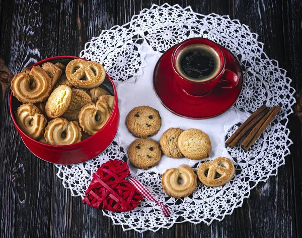 Cookies in a red box and a red cup of coffee and cinnamon on the table. Concept for National Cookie Day December 4 on wooden background.