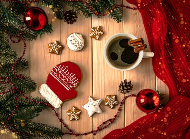 Noel arkaplanda kırmızı zencefilli ekmek ve bokeh efektli bir fincan kahve. Noel ağacı topları, dallar, kolye, koniler ve süs olarak kırmızı atkı..