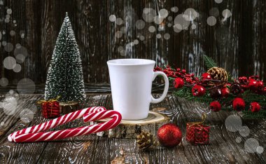 Beyaz bir fincan kahve ve koyu arkaplandaki masada kalp şeklinde kırmızı Noel lolipopları. Noel ağacı, toplar, kutsal dal, dekor olarak koniler..