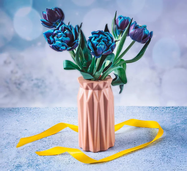 A bouquet of fresh blue tulip flowers in a pink vase. Still life with spring flowers on a light blue background.
