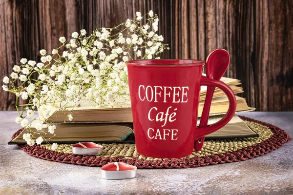 Still life with a red cup of coffee, books, gypsophila flowers, candles as decor. Close up view