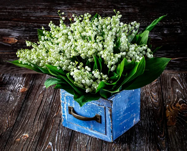 Bouquet of lily of the valley flowers in a blue wooden vintage box on a wooden background. View from above.