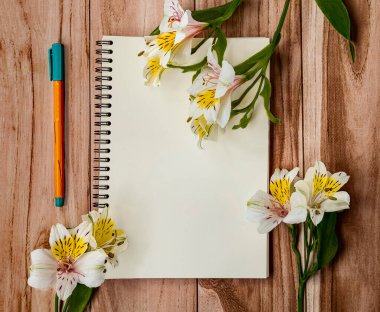 Açık defter, keçeli kalem ve çiçek buketinin en üst görüntüsü. Ofisi olan arka plan işyeri