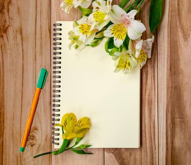 Açık defter, keçeli kalem ve çiçek buketinin en üst görüntüsü. Ofisi olan arka plan işyeri