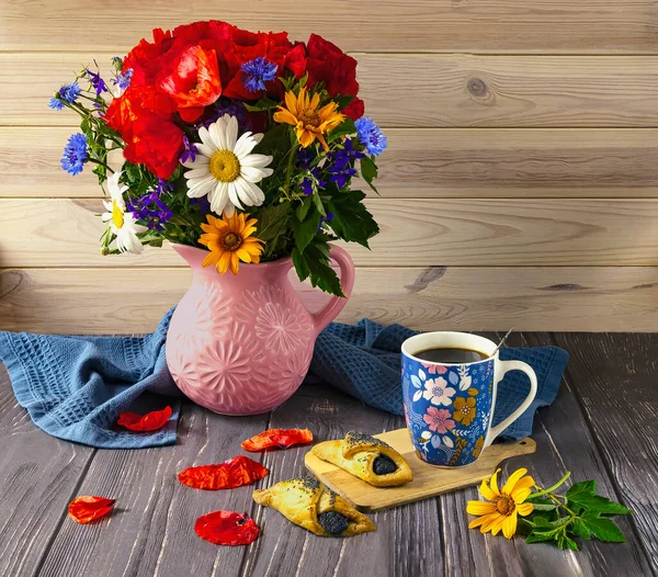 A bouquet of wildflowers with red poppies, a blue cup of coffee and poppy seed cookies on a wooden background. Summer still life