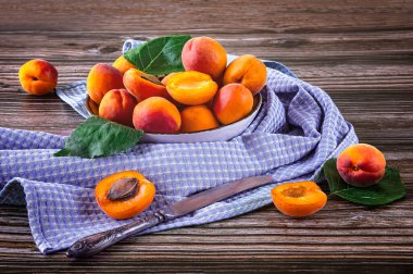 Tahta bir arka planda beyaz bir tabakta olgun kayısıları hasat et. Dekor olarak antika bıçak ve mavi masa örtüsü