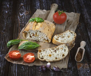 Taze kurutulmuş domatesli ciabatta, taze domates, yeşil fesleğen yaprağı, sarımsak ve baharat. Koyu bir ahşap arka planda kompozisyon.