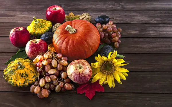 Autumn fruits and vegetables background. Harvest of ripe apples, grapes, plums, nuts and pumpkins on a dark wooden background. Side view