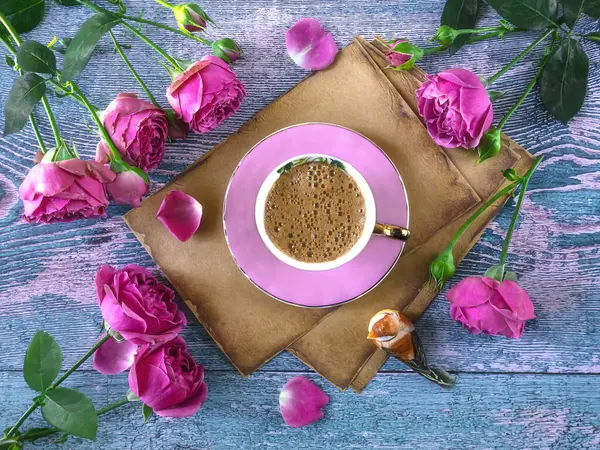 Pink coffee cup on old vintage paper, pink peony rose flowers on blue background. A romantic composition for Valentine\'s Day