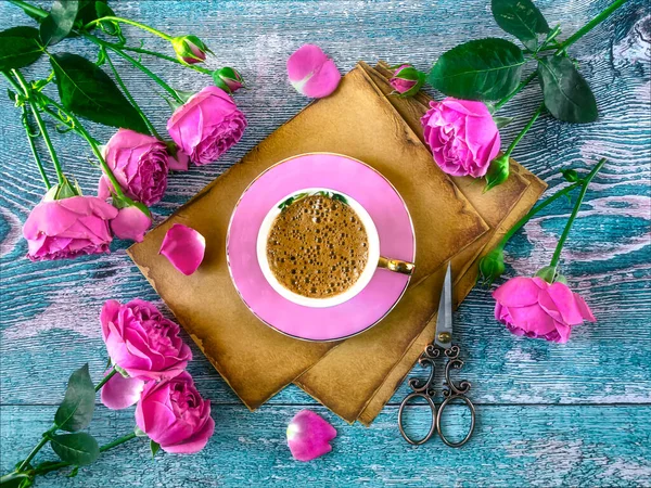 Pink coffee cup on old vintage paper, pink peony rose flowers on blue background. A romantic composition for Valentine\'s Day