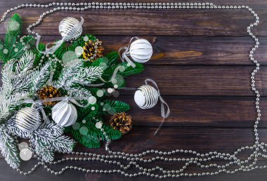 Noel arkaplanı beyaz Noel topları, Noel ağacı dalları, gümüş çelenkler ve çam kozalakları. Koyu ahşap arka planda şenlikli bir kompozisyon.