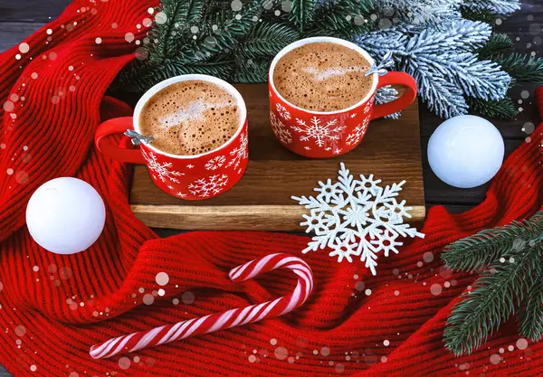 Christmas composition with two red coffee cups, snowflakes, lollipop, white candles, Christmas tree branches, red scarf on a snowy background.