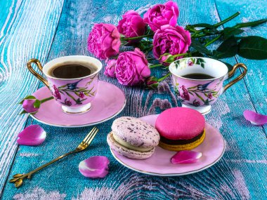 Makaronlar ve iki pembe kahve fincanı ve çiçek açan pembe güller, mavi arka planda kompozisyon.