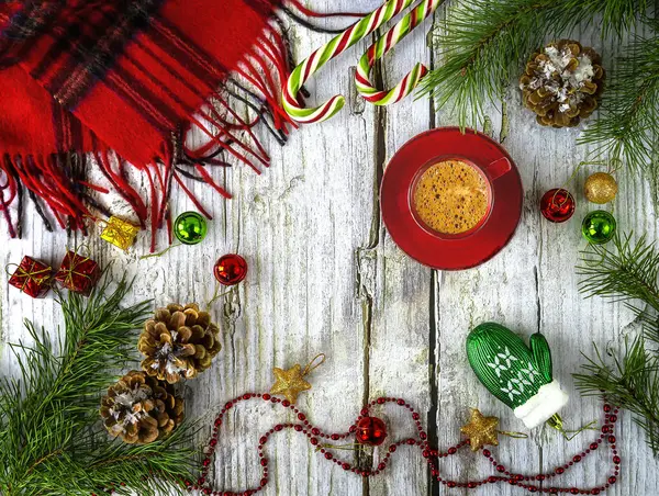 Hello winter background. Winter composition with a red cup of coffee, snowy pine branches, pine cones, Christmas tree toys and lollipops, a woolen scarf