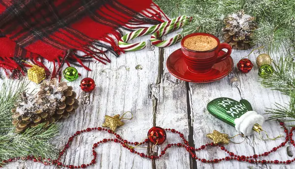Hello winter background. Winter composition with a red cup of coffee, snowy pine branches, pine cones, Christmas tree toys and lollipops, a scarf