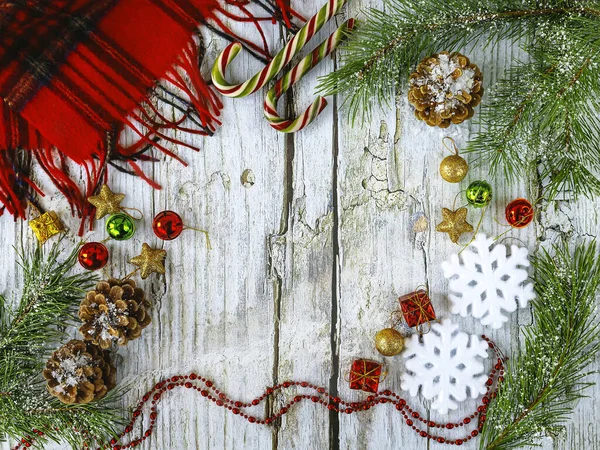 Hello winter background. Winter composition with snowy pine branches, cones, Christmas tree toys and lollipops, a scarf on a light wooden background.