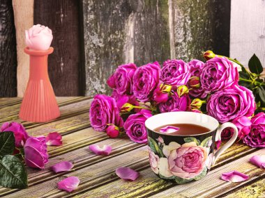 Bir buket pembe şakayık gülleri, güllerle süslenmiş bir fincan çay, gül şeklinde bir mum. Çiçeklerle romantik bir hayat