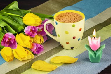 Bahar demeti pembe ve sarı lale çiçekleri, çiçek yaprakları, çizgili masa örtüsünün üzerindeki lale mumları. Bahar hala hayat
