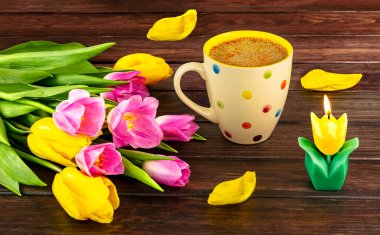 Bahar, beyaz bir benekli kahve, bir buket sarı ve pembe lale çiçekleri ve ahşap arka planda bir mum ile durgun bir hayattır..