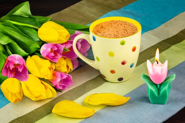 Bahar demeti pembe ve sarı lale çiçekleri, çiçek yaprakları, çizgili masa örtüsünün üzerindeki lale mumları. Bahar hala hayat