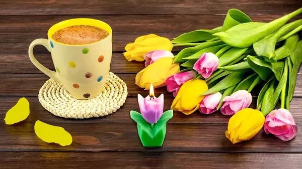 Bahar, beyaz bir benekli kahve, bir buket sarı ve pembe lale çiçekleri ve ahşap arka planda bir mum ile durgun bir hayattır..