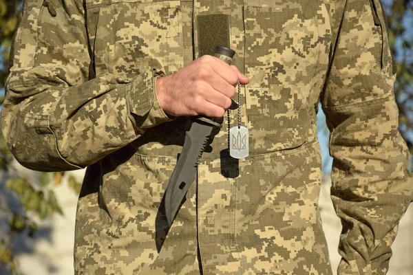 ウクライナ軍の男は トライデント ウクライナの紋章の紋章とナイフと軍事トークンを保持しています ウクライナでの戦争 — ストック写真