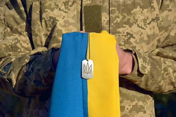 A Ukrainian military man holds the national flag in his hands as a symbol of strong. War in Ukraine. Day of the Cossacks and Defender of Ukraine.