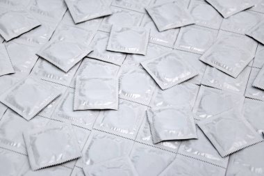 Arkaplan olarak bir sürü açılmamış prezervatif paketi. Hamilelik veya cinsel yolla bulaşan hastalıkları azaltmak için prezervatif kullanmak. Cinsel yolla bulaşan hastalıklar. Güvenli seks ve üreme sağlığı kavramı.