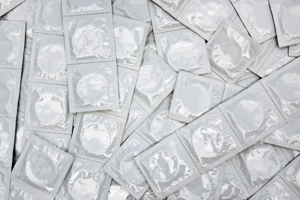 Many white packages of unopened condoms as a background. Using a condom to reduce the chance of pregnancy or sexually transmitted diseases, STDs. The concept of safe sex and reproductive health.