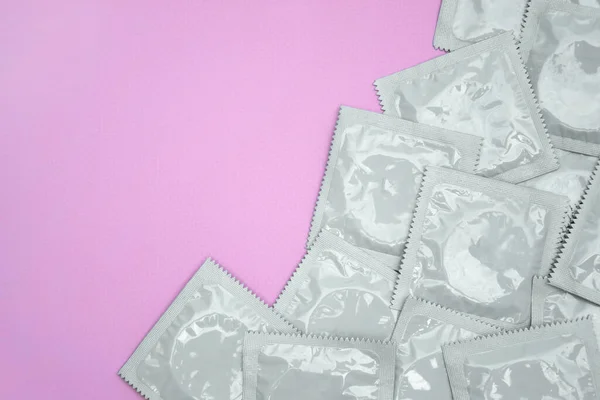 Many white packages of unopened condoms on a pink background. Using a condom to reduce the chance of pregnancy or sexually transmitted diseases, STDs. The concept of safe sex and reproductive health.