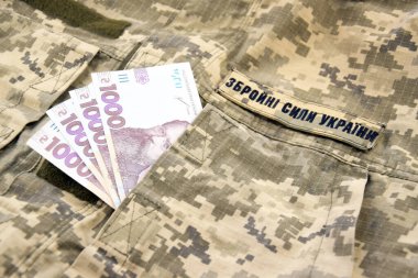 Ukrayna UAH askeri bir pikselin arka planına, Ukrayna askeri kuvvetlerinin üniformasına para yatırıyor. Maaş, ödeme ve orduya bağış kavramı.
