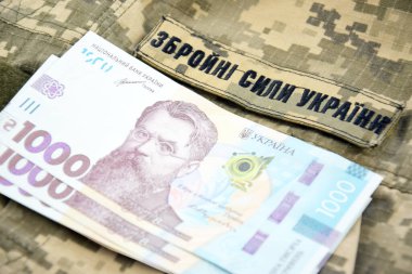 Ukrayna UAH askeri bir pikselin arka planına, Ukrayna askeri kuvvetlerinin üniformasına para yatırıyor. Maaş, ödeme ve orduya bağış kavramı.