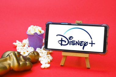KHARKIV, UKRAINE - JUNE 1, 2020: Smartphone with Disney studio logo, Oscar figure and popcorn. Film industry concept. clipart