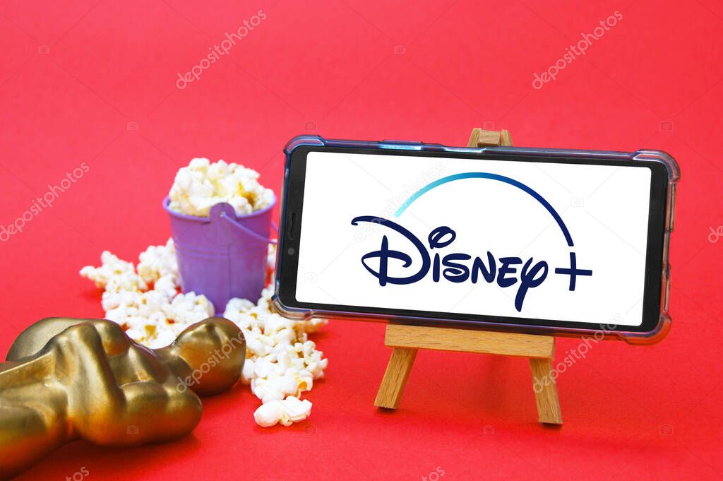 KHARKIV, UKRAINE - JUNE 1, 2020: Smartphone with Disney studio logo, Oscar figure and popcorn. Film industry concept.