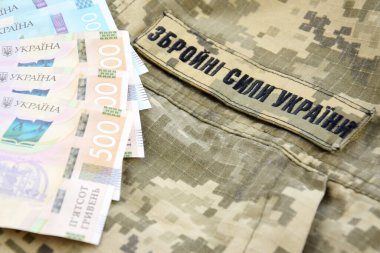 Ukrayna hrivnisi, Ukrayna silahlı kuvvetlerinin yazılı olduğu askeri bir pikselin arka planına karşı. Ücret, ödeme ve orduya bağış kavramı..