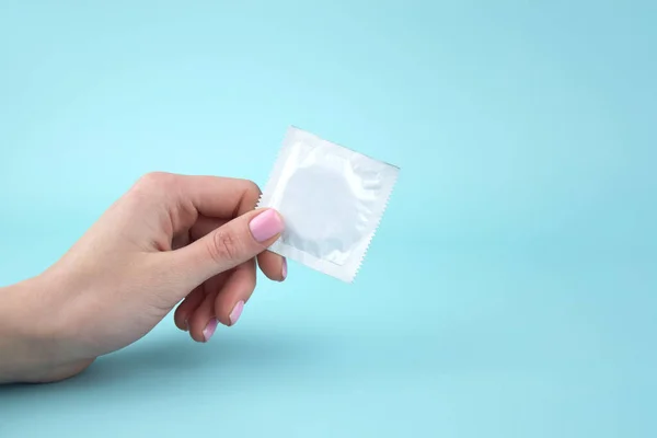 One white pack of condom in the girl's hand. Using a condom to reduce the chance of pregnancy or sexually transmitted diseases, STDs. The concept of safe sex and reproductive health.