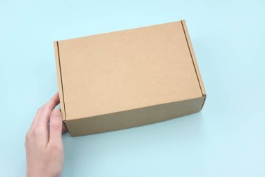 Kadın eli, doğal kıvrımlı kartondan yapılmış kahverengi ekolojik paket kutusunu tutuyor. Paketleme, alışveriş, teslimat konsepti.
