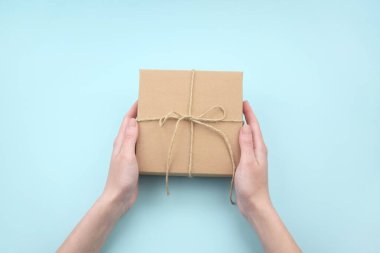 Kadın eli, doğal kıvrımlı kartondan yapılmış kahverengi ekolojik paket kutusunu tutuyor. Paketleme, alışveriş, teslimat konsepti.