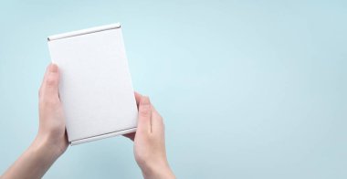 Mavi arka planda beyaz paket kutusunu tutan kadın eller. Paketleme, alışveriş, teslimat konsepti.
