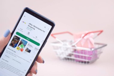 Kharkiv, Ukrayna, 31 Mart 2023: Akıllı telefonlu alışveriş arabası pembe arka planda Ebay uygulamasını açtı.